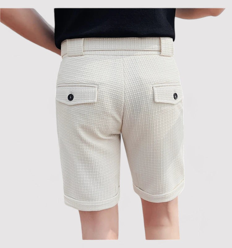 Short beige shorts en tissu texturé avec poches arrière à boutons noirs, portés par une personne de dos. Mode estivale élégante et décontractée.