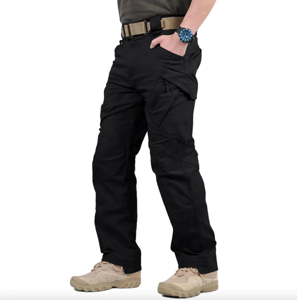 Pantalon tactique noir pour homme avec poches multiples, ceinture robuste et chaussures de randonnée beige. Idéal pour activités extérieures et survie.