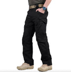 Pantalon tactique noir pour homme avec poches multiples, ceinture robuste et chaussures de randonnée beige. Idéal pour activités extérieures et survie.