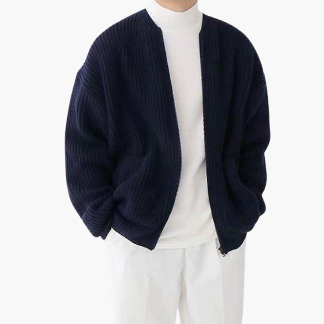 Homme portant un cardigan bleu marine en maille côtelée sur un col roulé blanc, pantalon blanc. Mode masculine élégante et décontractée.
