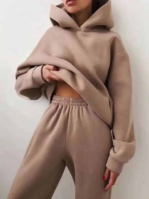 Femme portant un ensemble de survêtement beige, composé d'un sweat à capuche ample et d'un pantalon confortable. Mode décontractée tendance.