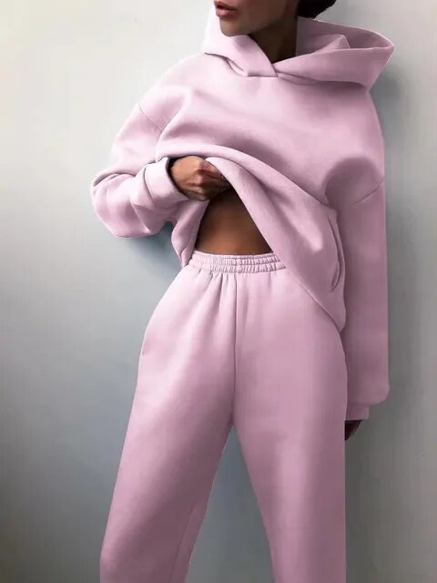 Personne portant un ensemble de survêtement rose pastel, composé d'un sweat à capuche et d'un pantalon de jogging, mode décontractée tendance.