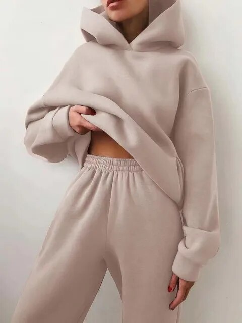 Femme portant un ensemble de survêtement beige, composé d'un sweat à capuche et d'un pantalon ample. Mode décontractée, tendance automne-hiver.