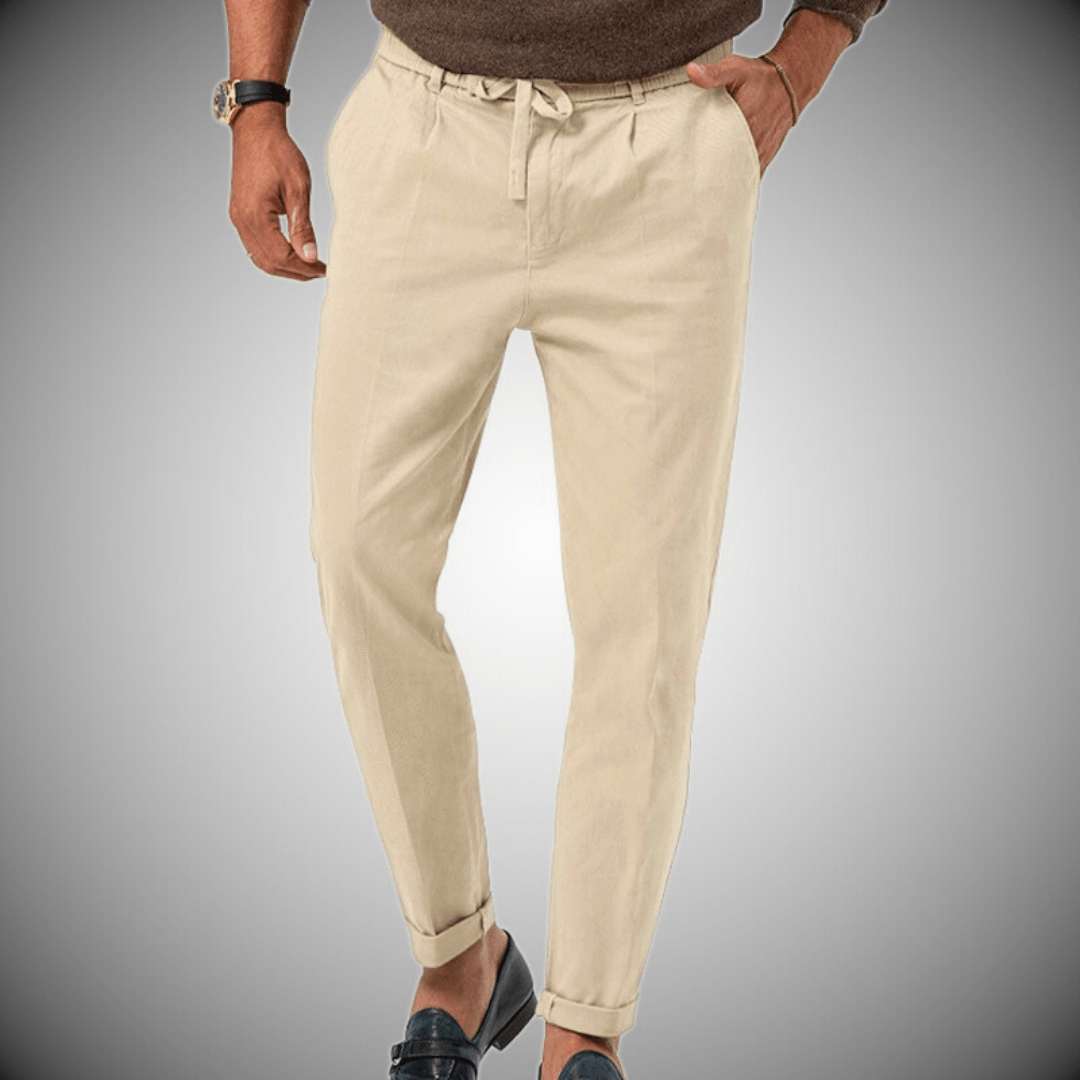 Pantalon beige homme élégant, coupe ajustée, avec ceinture à cordon, porté avec des mocassins noirs et un pull marron. Mode masculine chic.