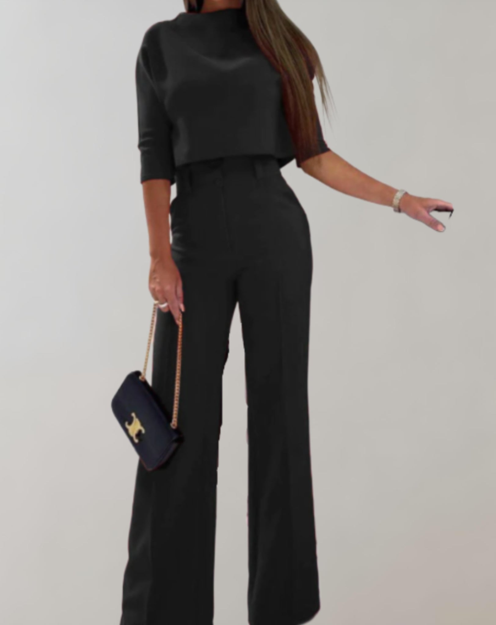 Femme en tenue élégante noire, portant un sac à main chic, posant contre un fond neutre. Mode féminine, style sophistiqué, vêtements tendance.