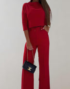Femme en ensemble rouge élégant, pantalon large et haut à manches trois-quarts, tenant un sac à main noir avec chaîne dorée. Mode chic et tendance.