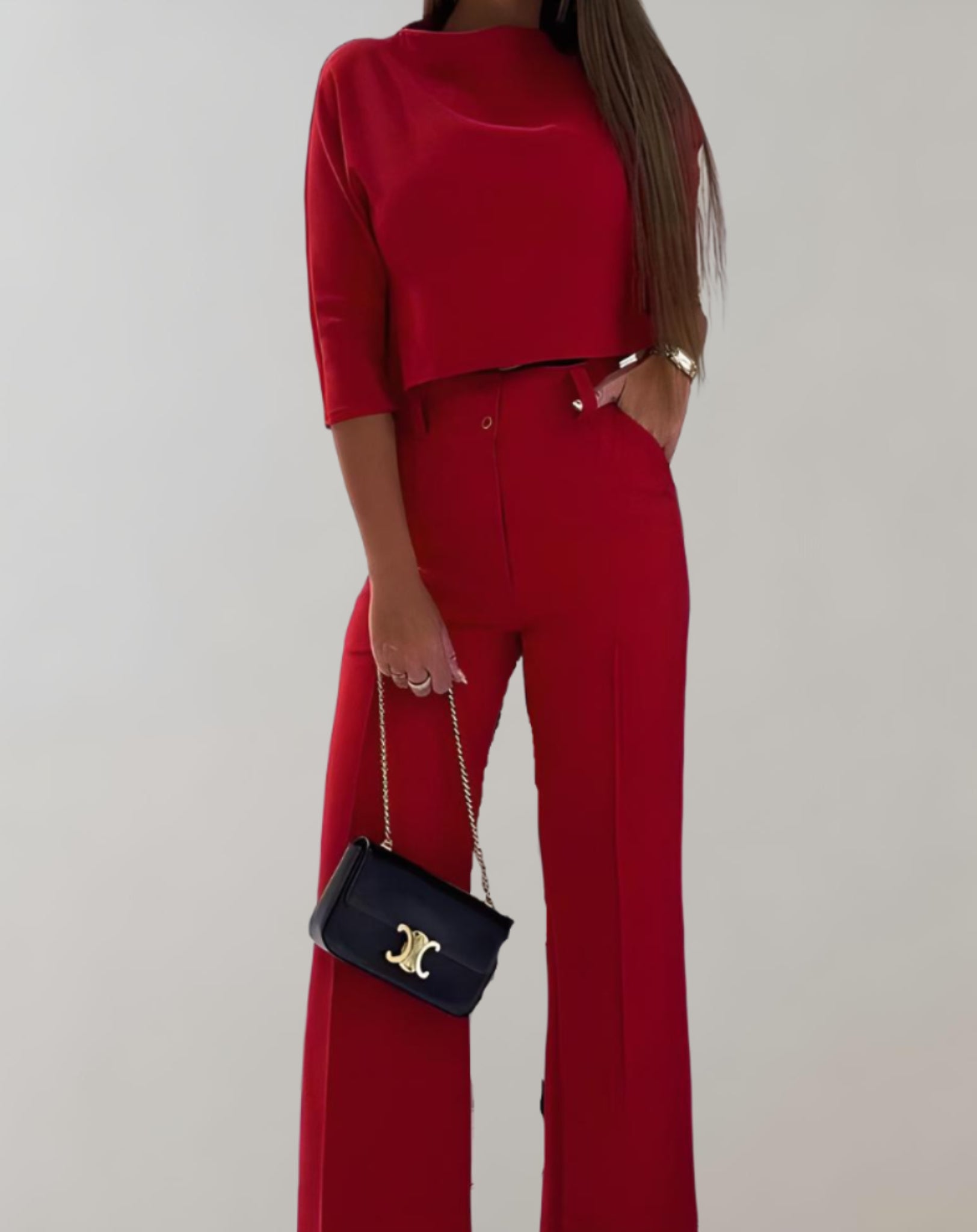 Femme en ensemble rouge élégant, pantalon large et haut à manches trois-quarts, tenant un sac à main noir avec chaîne dorée. Mode chic et tendance.