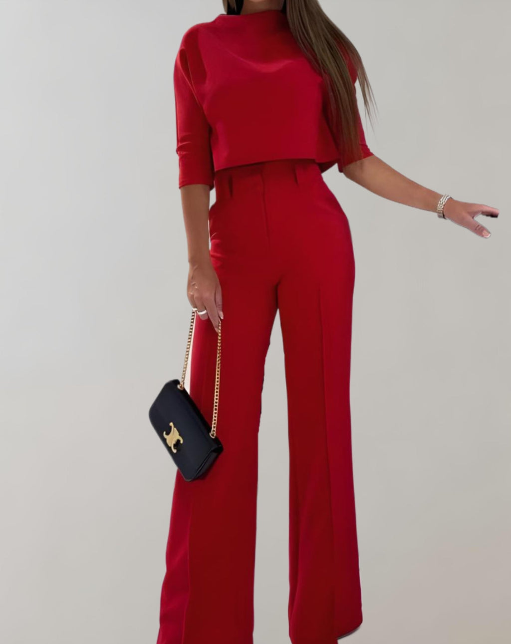 Femme en ensemble rouge élégant, pantalon large et haut à manches trois-quarts, tenant un sac à main noir avec chaîne dorée. Mode chic et moderne.