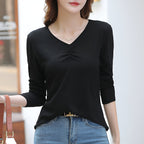 Femme portant un t-shirt noir à manches longues, col en V, avec un jean bleu. Mode décontractée, élégance simple, style urbain.