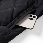 Smartphone moderne argenté dans une poche de veste noire matelassée avec fermeture éclair, design élégant, technologie mobile, accessoire quotidien.