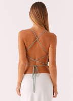 Femme de dos portant une robe dos nu avec bretelles croisées, cheveux longs et lisses, fond blanc. Mode élégante, style estival.