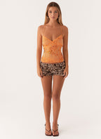 Jeune femme portant un haut orange à motifs et un short léopard, debout sur fond blanc. Mode féminine, tenue estivale tendance.