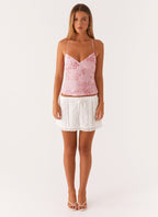 Jeune femme portant un haut rose à bretelles et une jupe blanche en dentelle, posant sur fond blanc. Mode féminine, tenue estivale élégante.