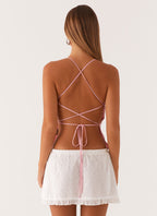 Femme de dos portant une robe d'été dos nu rose avec jupe blanche en dentelle, cheveux longs, style estival, mode féminine tendance.