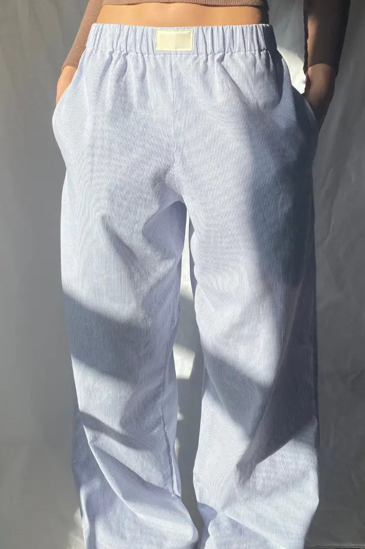 Pantalon ample à rayures bleues et blanches, style décontracté, avec poches latérales, éclairé par la lumière naturelle. Mode tendance et confortable.