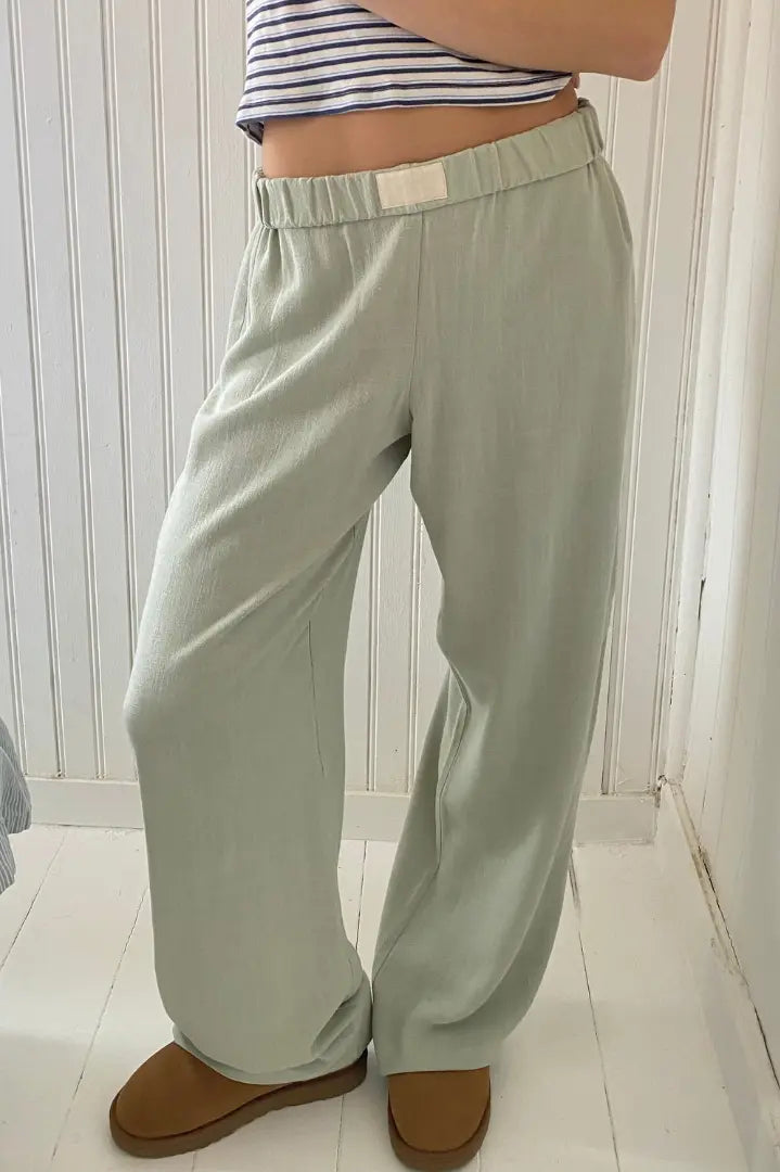 Pantalon ample vert clair en lin, taille élastique, porté par une personne avec un haut rayé. Mode décontractée, confort, style estival.