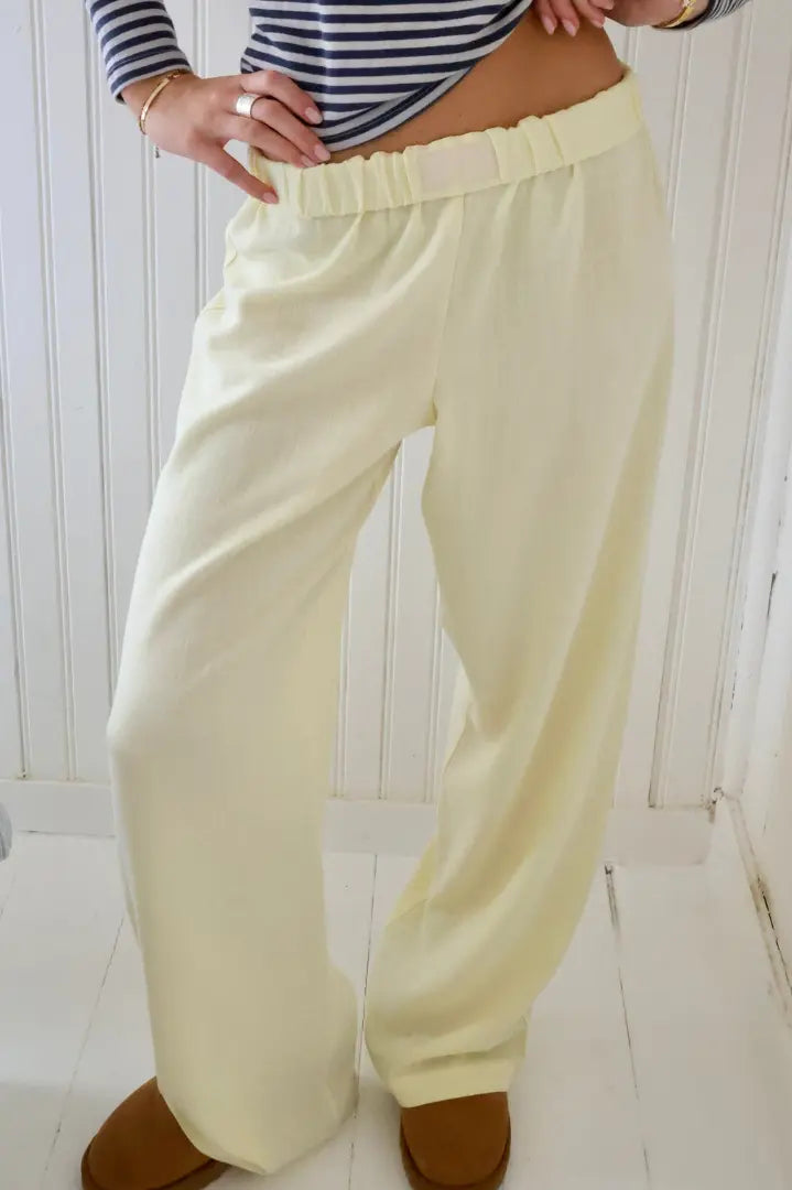 Pantalon ample jaune clair en lin, taille élastique, porté par une personne avec un haut à rayures marinières, sur fond de mur blanc.