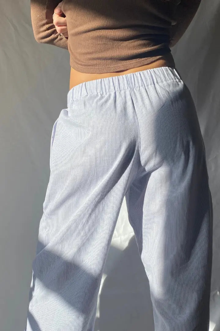 Femme portant un pantalon ample à rayures bleues et blanches, taille élastique, avec un haut marron ajusté. Mode décontractée, style minimaliste.