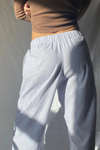 Femme portant un pantalon ample à rayures bleues et blanches, taille élastique, avec un haut marron ajusté. Mode décontractée, style minimaliste.