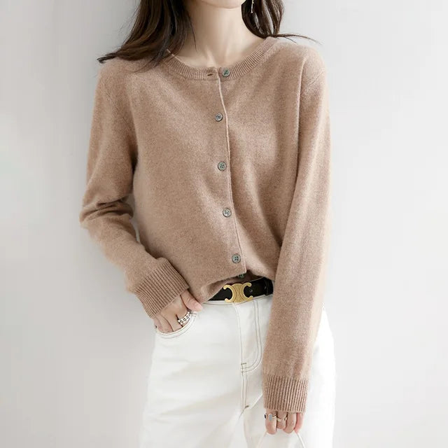 Femme portant un cardigan beige en cachemire avec boutons, associé à un pantalon blanc. Mode élégante et confortable pour l'automne.