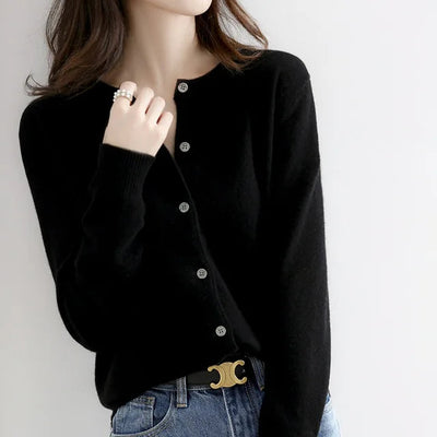 Femme portant un cardigan noir boutonné, jean bleu et ceinture avec boucle dorée. Mode élégante, tenue décontractée chic, style automne-hiver.