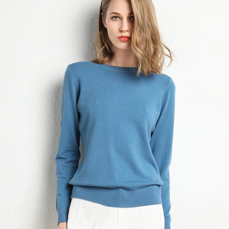 Jeune femme portant un pull bleu élégant, manches longues, sur fond blanc. Mode féminine, style décontracté, tendance automne-hiver.