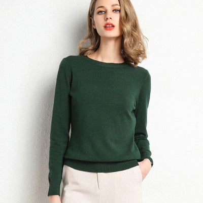 Jeune femme portant un pull vert élégant, manches longues, posant contre un mur blanc. Mode féminine, style automne-hiver, tenue décontractée chic.