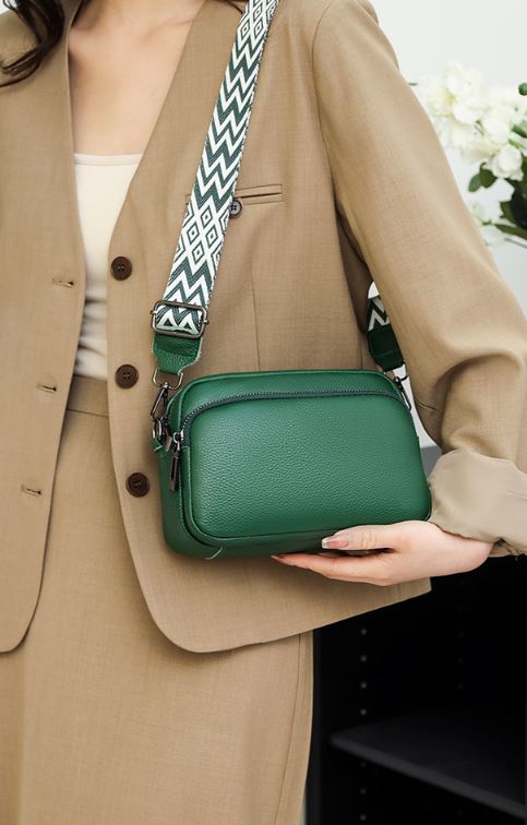 Sac à main vert en cuir avec bandoulière à motifs géométriques, porté par une femme en tailleur beige. Accessoire mode élégant et tendance.