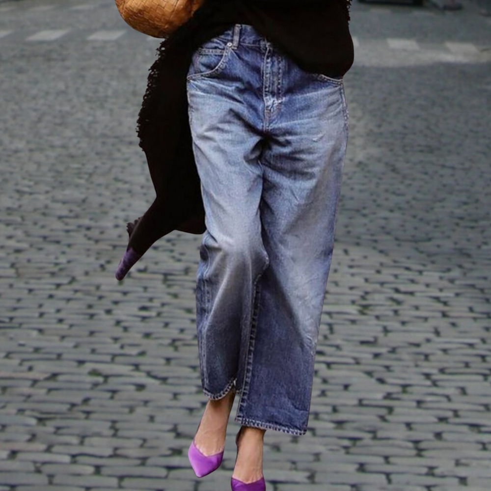 Jeans larges en denim bleu portés avec des talons violets sur une rue pavée. Mode urbaine, style décontracté, tendance automne.