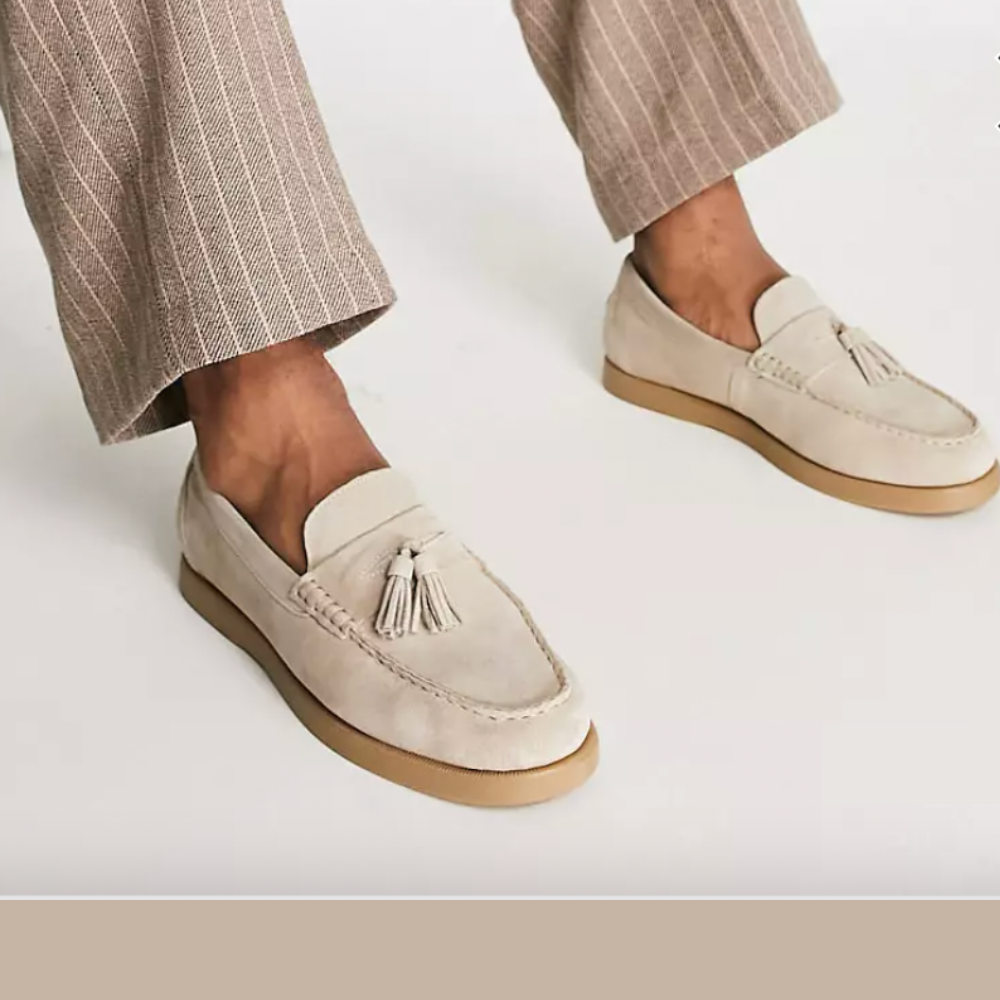 Chaussures mocassins beige en daim avec pampilles, portées avec un pantalon à rayures marron clair. Style élégant et décontracté pour homme.