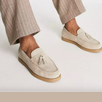 Chaussures mocassins beige en daim avec pampilles, portées avec un pantalon à rayures marron clair. Style élégant et décontracté pour homme.
