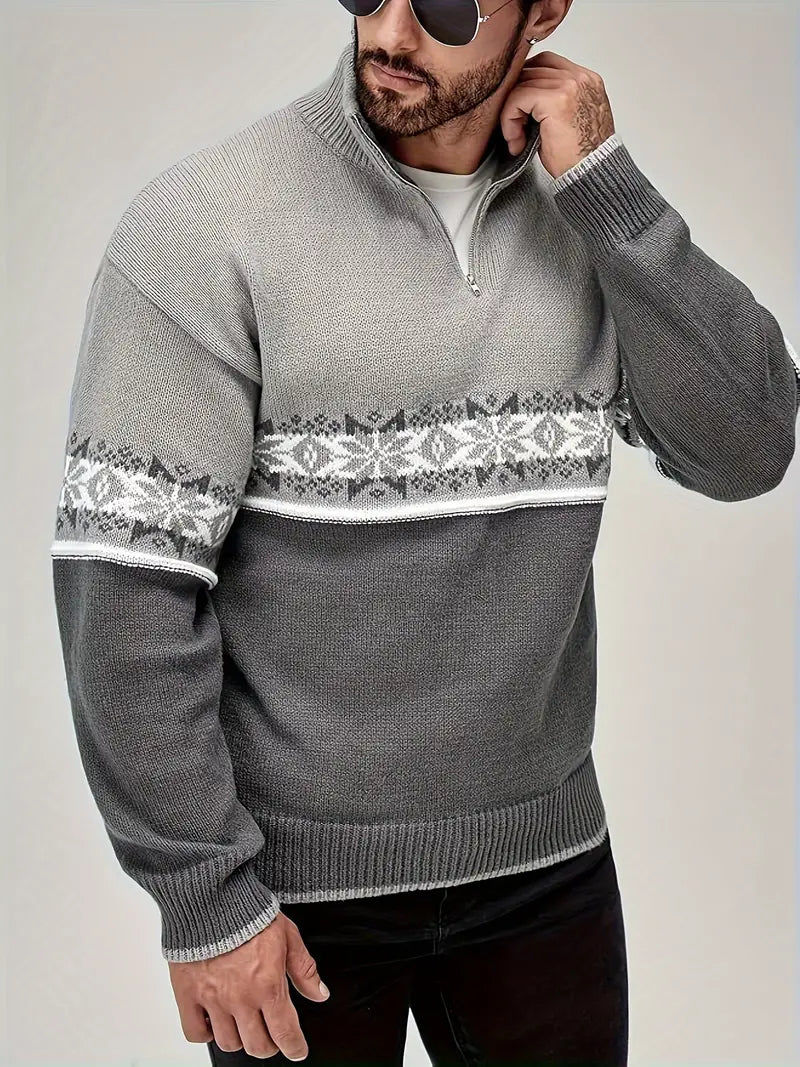 Homme portant un pull gris à col zippé avec motif nordique blanc et noir, lunettes de soleil, sur fond neutre. Mode hiver, style décontracté.