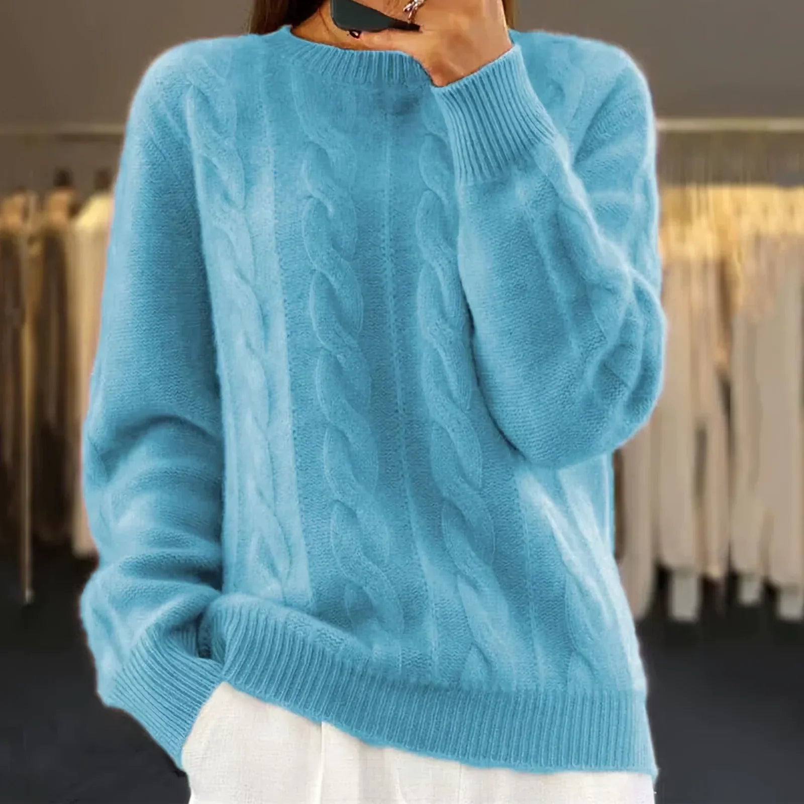 Femme portant un pull bleu en laine torsadée, manches longues, col rond, dans un dressing moderne. Mode hiver, vêtement chaud et élégant.