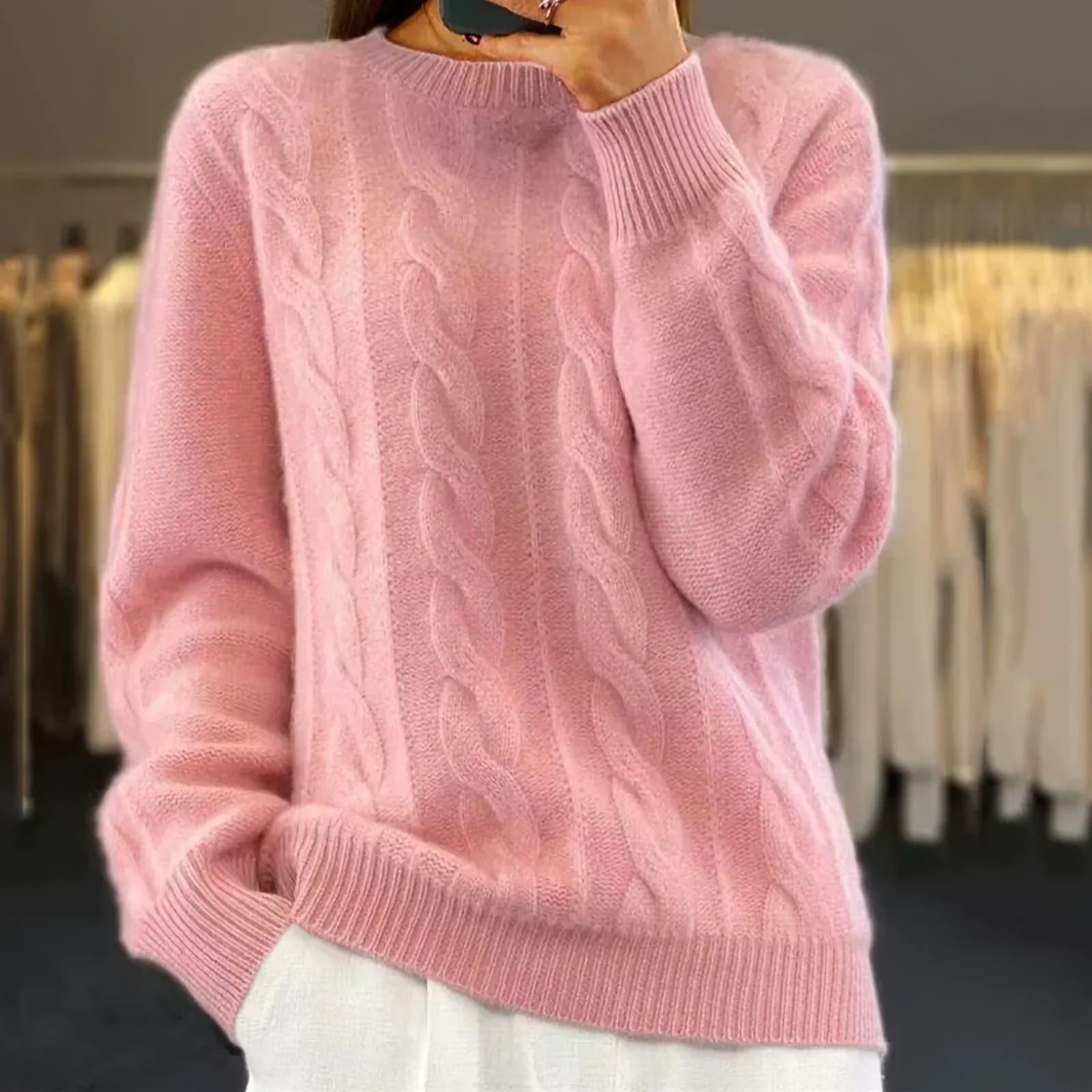 Femme portant un pull rose en maille torsadée, manches longues, dans une boutique de vêtements. Mode féminine, tendance automne-hiver.