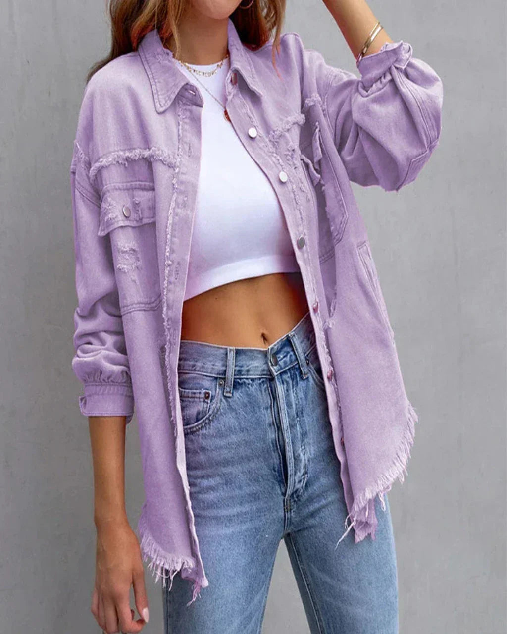 Femme portant une chemise en jean violet délavé, effilochée, avec un crop top blanc et un jean bleu. Mode décontractée, tendance urbaine.
