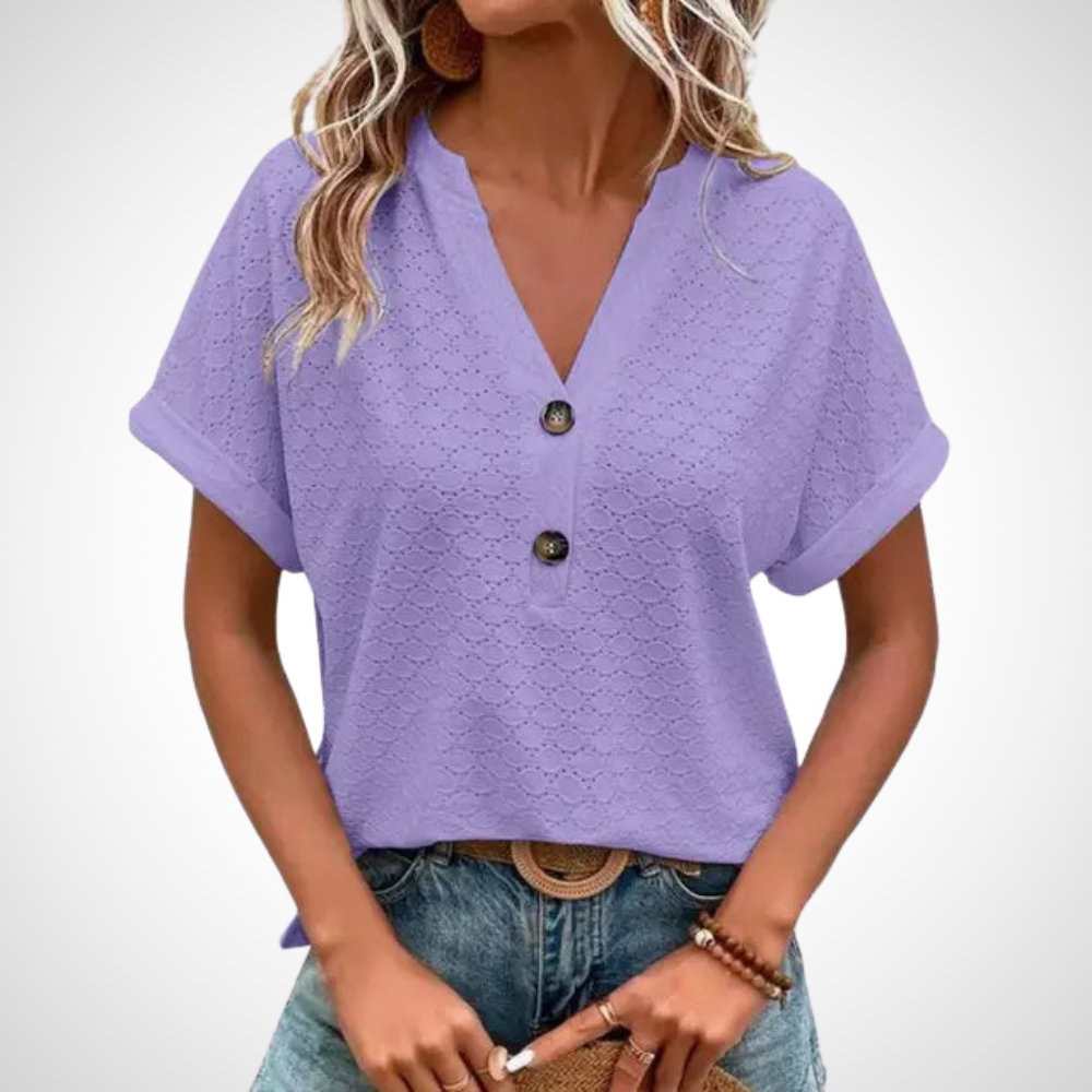 Blouse violette en dentelle avec manches courtes, col en V et boutons décoratifs, portée par une femme avec un jean. Mode féminine élégante.