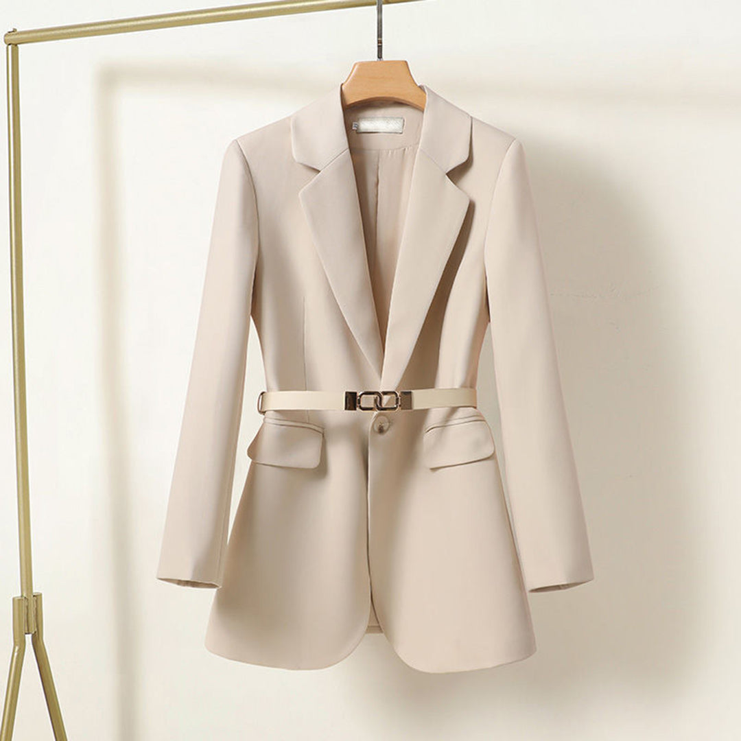 Blazer beige élégant pour femme avec ceinture, suspendu sur un cintre. Veste moderne, mode féminine, tenue professionnelle chic.