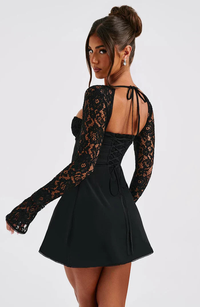 Femme portant une robe noire en dentelle avec manches longues, dos nu et lacets. Mode élégante, tenue de soirée chic, style tendance.