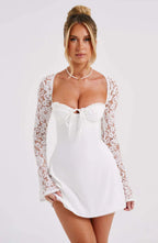 Robe blanche élégante avec manches en dentelle, décolleté en cœur et nœud central, portée par une femme. Mode féminine chic et tendance.