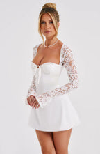 Robe blanche élégante avec manches en dentelle, décolleté en cœur, portée par une femme souriante. Mode féminine, tenue chic, style moderne.