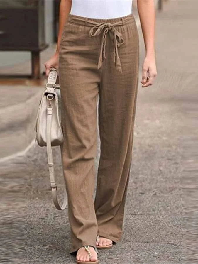 Pantalon large en lin marron avec ceinture nouée, porté par une femme tenant un sac beige, mode décontractée estivale, rue pavée.
