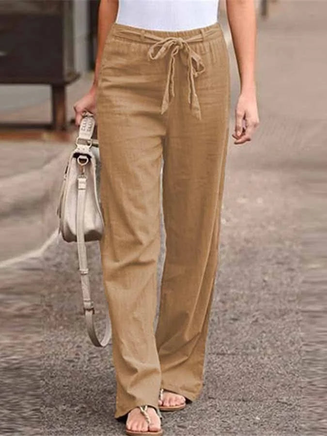 Pantalon large en lin beige avec ceinture à nouer, porté par une femme, accompagné d'un sac à main gris. Mode décontractée, tendance estivale.