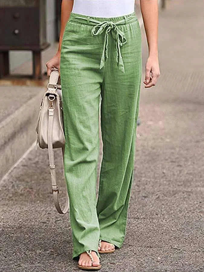 Pantalon vert en lin pour femme, taille haute avec ceinture nouée, porté avec un débardeur blanc et des sandales, style décontracté estival.