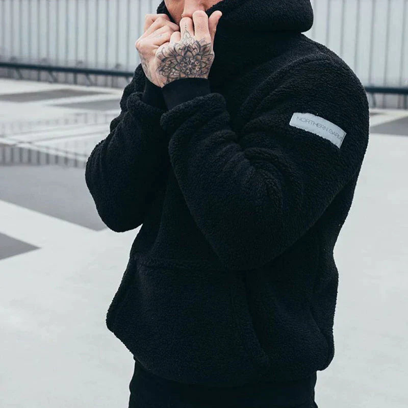 Homme en veste polaire noire, tatouage sur la main, extérieur urbain. Mode hiver, style décontracté, tendance vêtements chauds.