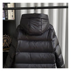 Doudoune noire à capuche suspendue sur un cintre, devant un rideau blanc. Veste d'hiver chaude, tendance, idéale pour le froid.