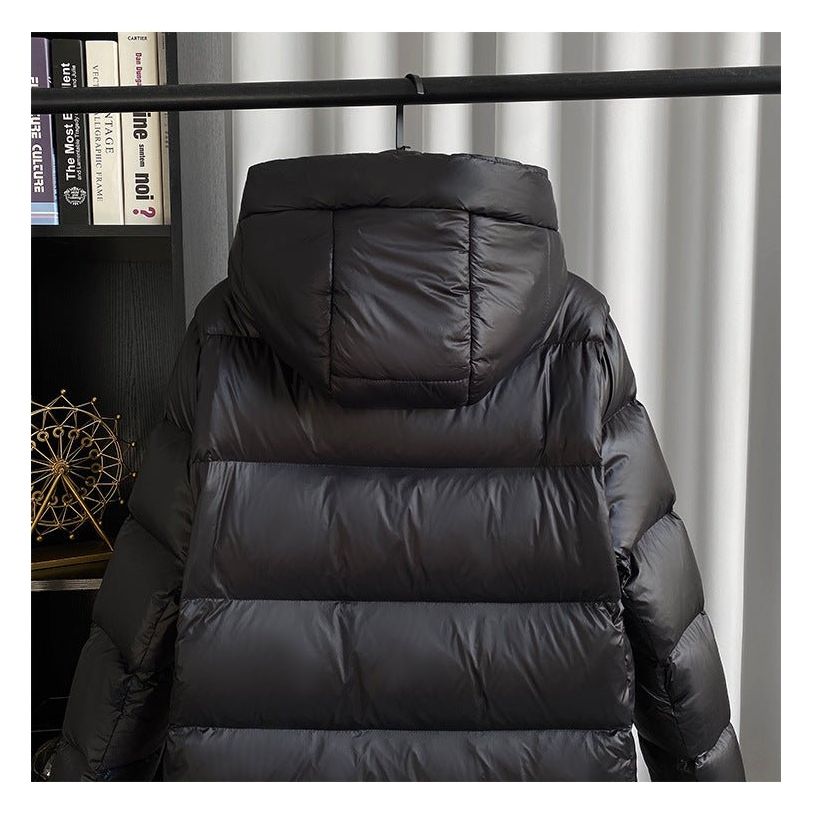 Doudoune noire à capuche suspendue sur un cintre, devant un rideau blanc. Veste d'hiver chaude, tendance, idéale pour le froid.