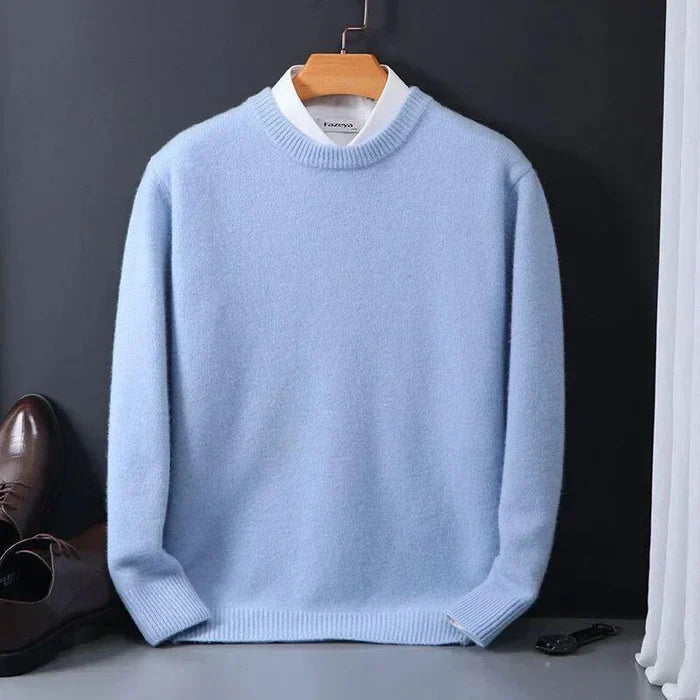 Pull bleu clair en laine sur cintre, chemise blanche en dessous, posé sur fond noir avec chaussures marron à côté. Mode homme élégante et chic.