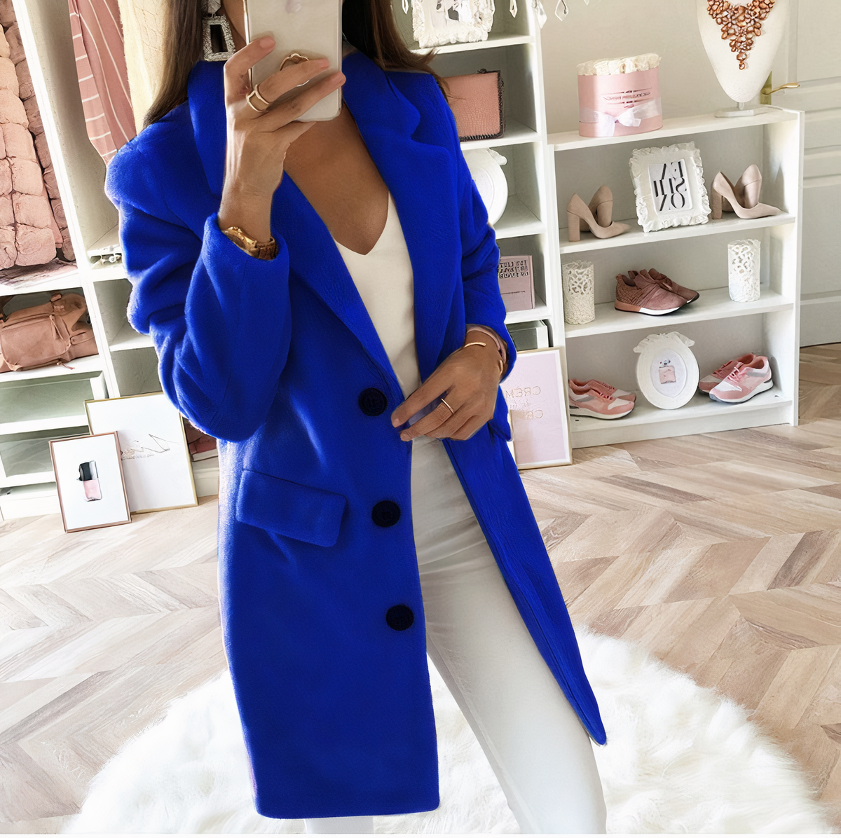 Femme en manteau bleu vif, posant dans un dressing moderne avec vêtements et accessoires de mode. Style élégant, tendance automne-hiver.
