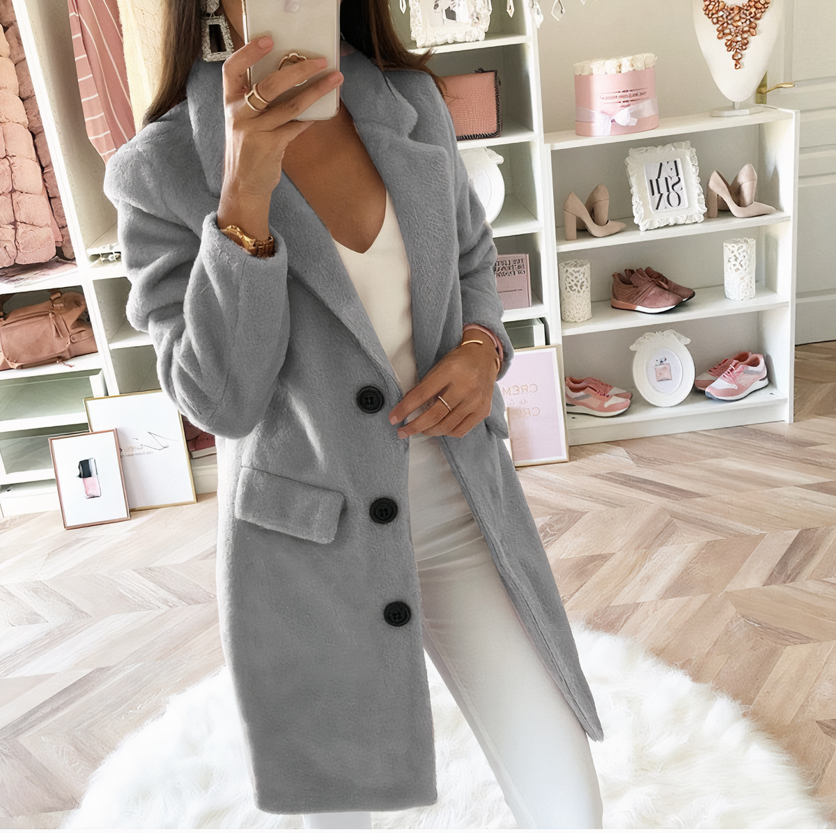 Femme en manteau gris élégant, posant dans un dressing moderne avec étagères blanches, vêtements et accessoires de mode. Style chic et tendance.