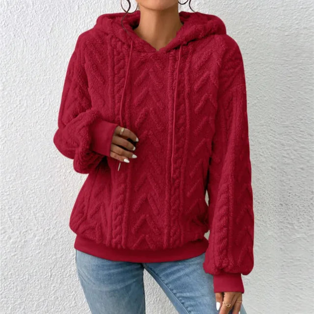 Femme portant un pull à capuche rouge texturé, manches longues, sur fond blanc. Mode automne, style décontracté, tendance vêtements chauds.